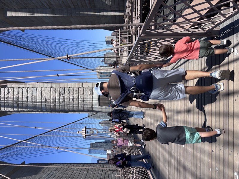 Mason walking across the Brooklyn Bridge holding his kids' hands